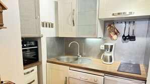 Une cuisine de taille réduite, dotée de meubles blancs, d’un évier en acier inoxydable, d’une machine à café et d’un lave-vaisselle.