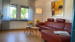 Una sala de estar moderna con un sofá de cuero, una mesita de madera con un jarrón de girasoles y un ventanal con vistas a árboles.