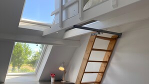 Un dormitorio tipo loft con un tragaluz, una escalera de madera, un escritorio y una silla.