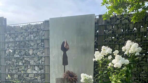 Un jardín con una estructura de concreto, una cerca de metal y diversas plantas.