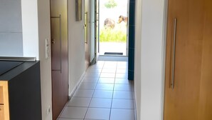 Un pasillo con una zona de cocina a la izquierda, una puerta de madera a la derecha y vistas al exterior.