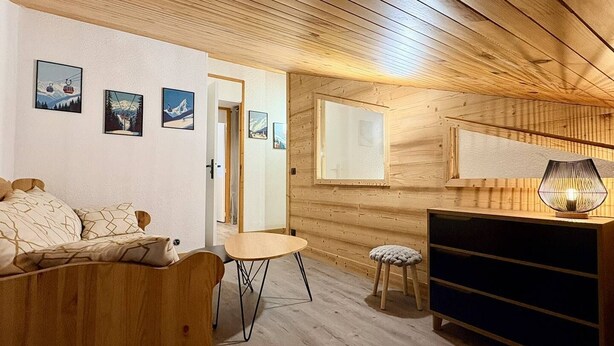 Ett mysigt rum med ett träpanelat tak, en säng, ett litet bord, en pall och ett TV-bord.