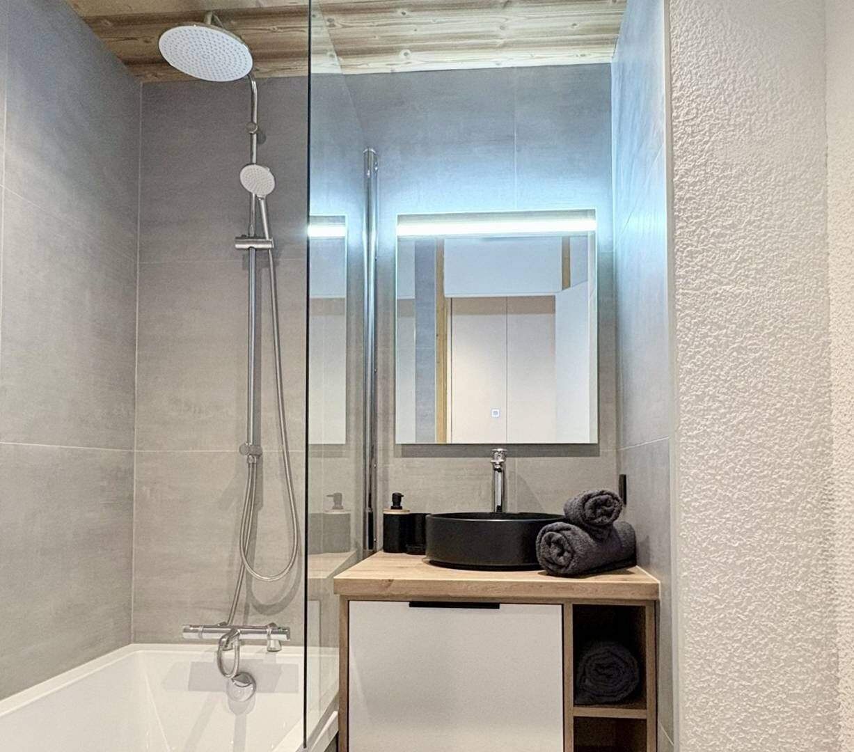 Ein modernes Badezimmer mit einer gläsernen Duschkabine, einer weißen Badewanne und einem Holzwaschtisch.