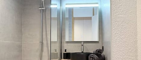 A modern bathroom with a glass-enclosed shower, a white bathtub, and a wooden vanity with a sink.