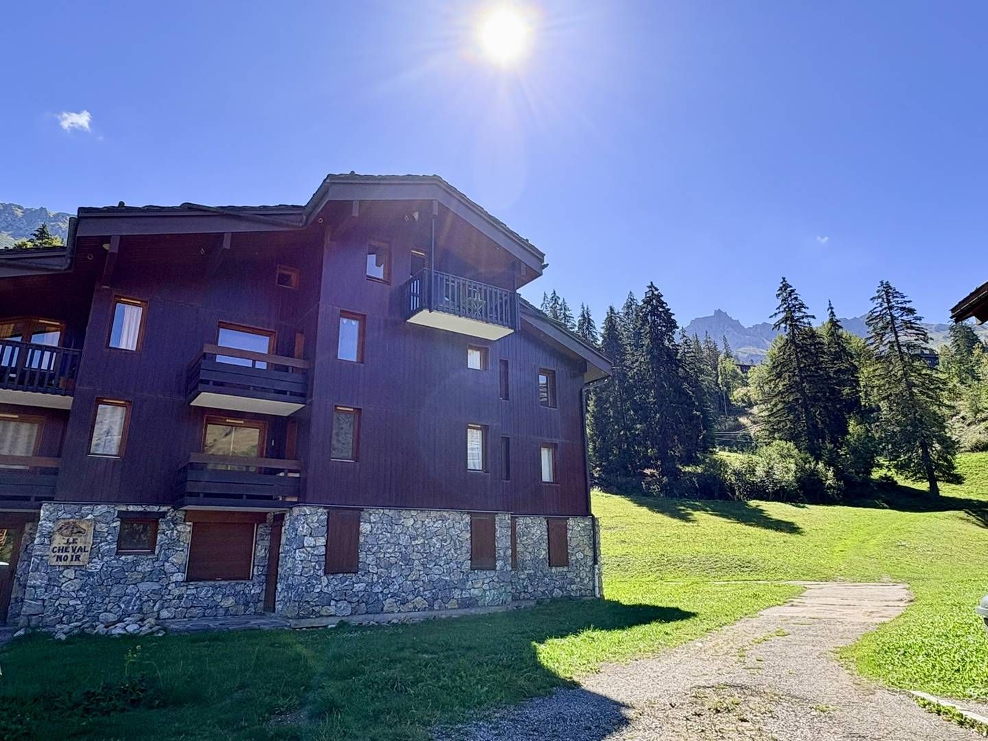 A multi-story building with a stone base, balconies, and a clear view of the surrounding mountains.