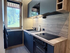 A modern kitchen with a large window, dark cabinetry, and a wooden backsplash. - Cheval Noir 32 - Charming 3-room apartment (LES AVANCHERS VALMOREL)