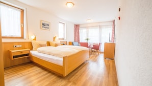 A room with a wooden bed, bedside table, and a small desk with a chair. - Hotel-Pension Enzian – Double Room with Balcony or Terrace, Breakfast Included (Todtnau)
