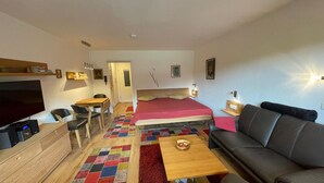 A compact hotel room with a bed, a sofa, a TV, a desk, and a small table. - Studio 'Inzell mit Mountain View' with Balcony and Wi-Fi (Inzell)