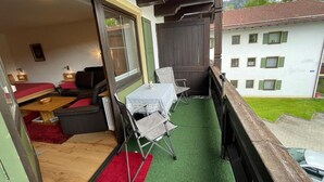 A balcony with a table and chairs, a sofa, and a view of a building with windows. - Studio 'Inzell mit Mountain View' with Balcony and Wi-Fi (Inzell)