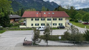 A two-story building with a red-tiled roof, multiple windows, and a parking area with cars. - Studio 'Inzell mit Mountain View' with Balcony and Wi-Fi (Inzell)
