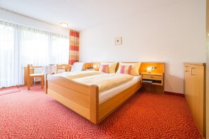 Ett hotellrum med en säng i trä, ett skrivbord, en stol, ett nattduksbord med en lampa och en garderob.