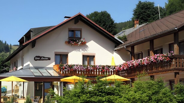 A building with a sign reading 'Haus Gvion,' a balcony with flowers, and outdoor seating with umbrellas. - Hotel-Pension Enzian: Double Room with Balcony or Terrace, Breakfast Included (Todtnau)