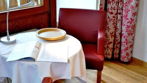 A room with a round table, a red chair, a book, and a menu. - Hotel-Pension Enzian: Double Room with Balcony or Terrace, Breakfast Included (Todtnau)