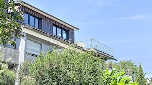 Une maison moderne à deux étages, dotée d’un balcon, de grandes fenêtres et d’un garage.