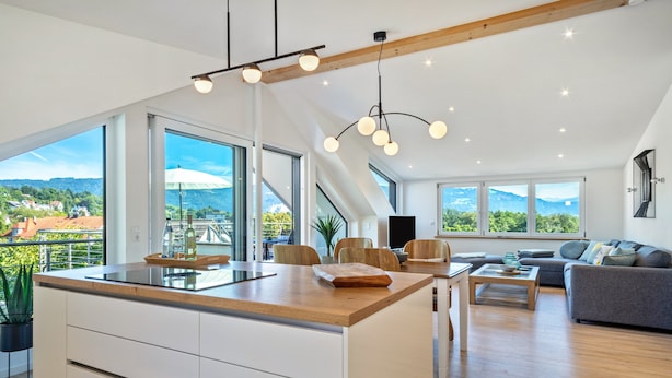 Une cuisine moderne dotée d’un grand îlot central, d’un coin repas avec des chaises, d’un canapé et offrant une vue sur les montagnes.
