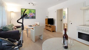 En stue med et løbebånd, en sofa, et fjernsyn, en vinflaske og glas på et bord.
