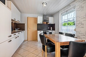 Une cuisine moderne avec des meubles blancs, une table à manger en bois et une fenêtre donnant sur un paysage verdoyant.