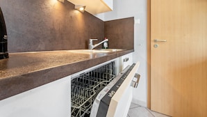 A modern kitchen with a dishwasher, a sink, and a wooden door. - Apartment 'Gemütliche' with Shared Terrace, Shared Garden and Wi-Fi (Cuxhaven)