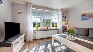 A living room with a television, sofa, coffee table, and potted plants by a window. - Apartment 'Gemütliche' with Shared Terrace, Shared Garden and Wi-Fi (Cuxhaven)