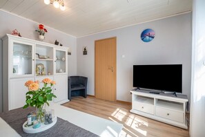 Un salon avec un téléviseur, un meuble avec des portes en verre, une porte et un mur orné d’un tableau.