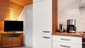 Una habitación con techo de madera, un televisor sobre un mueble de madera, una cafetera en la encimera y una puerta blanca.