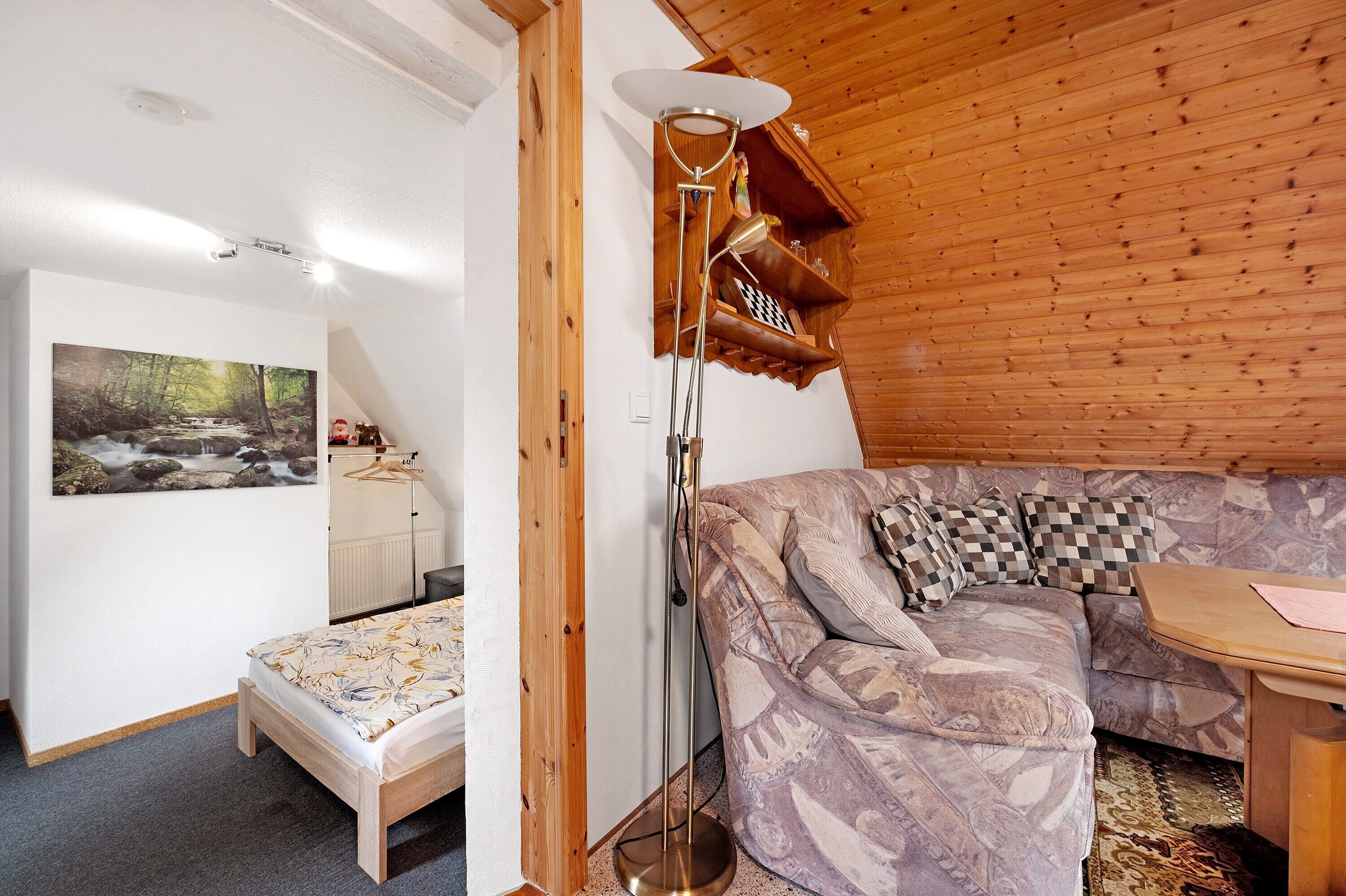 Ett mysigt rum med ett träpanelat tak, en soffa, ett litet bord och en golvlampa.