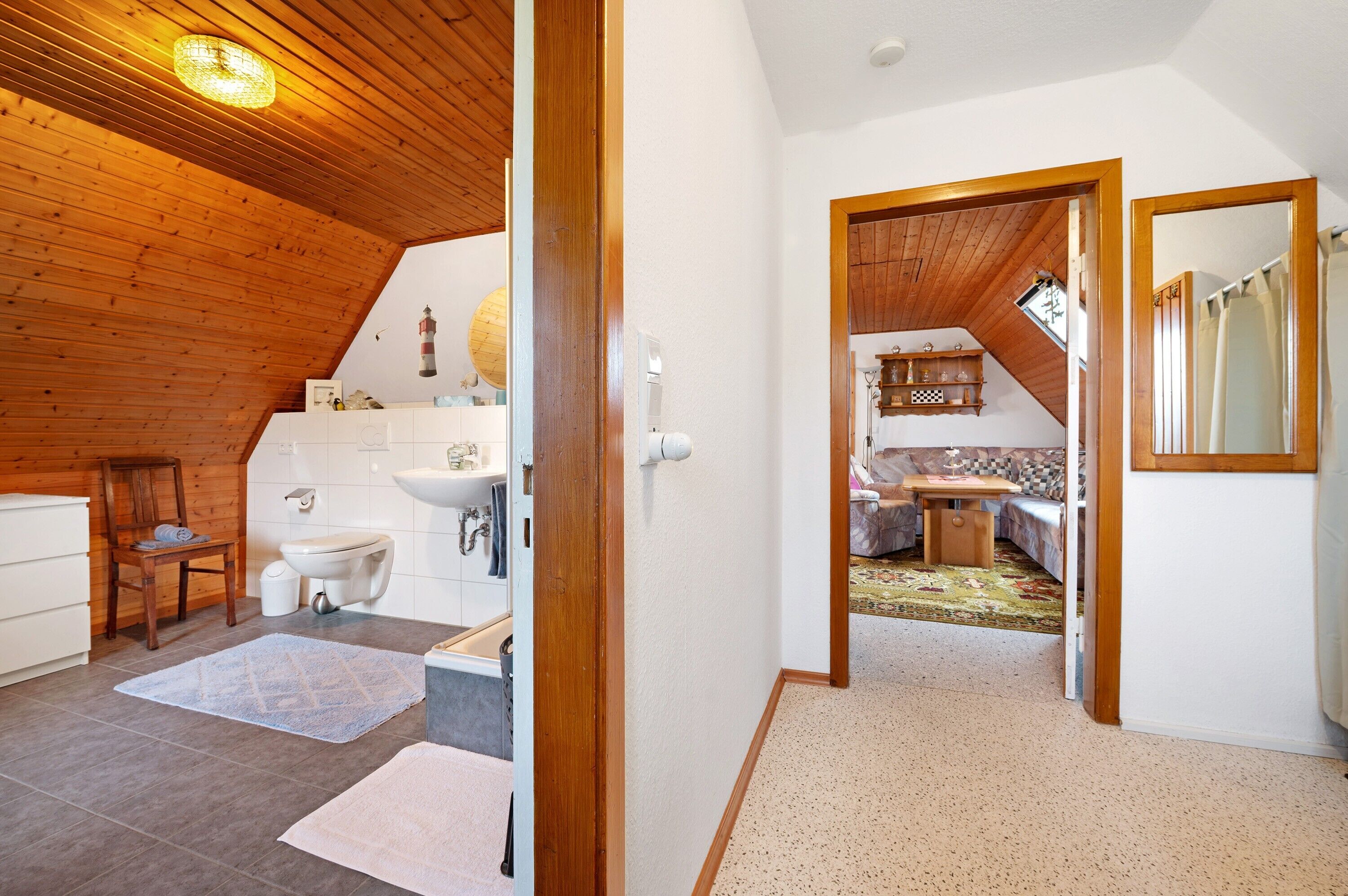 Een kamer met een houten plafond, een witte wastafel, een stoel en een klein tafeltje.