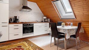 Una cocina con armarios blancos, estufa y microondas. Hay una mesa de comedor con sillas y una ventana encima.