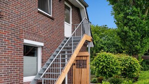 Un edificio de ladrillo con una escalera metálica que conduce a una puerta de madera, rodeado de follaje.