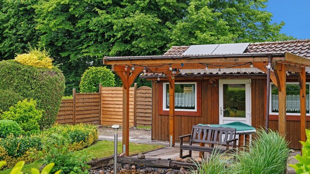 Una cabaña de madera con un patio, un pequeño estanque y una banca.