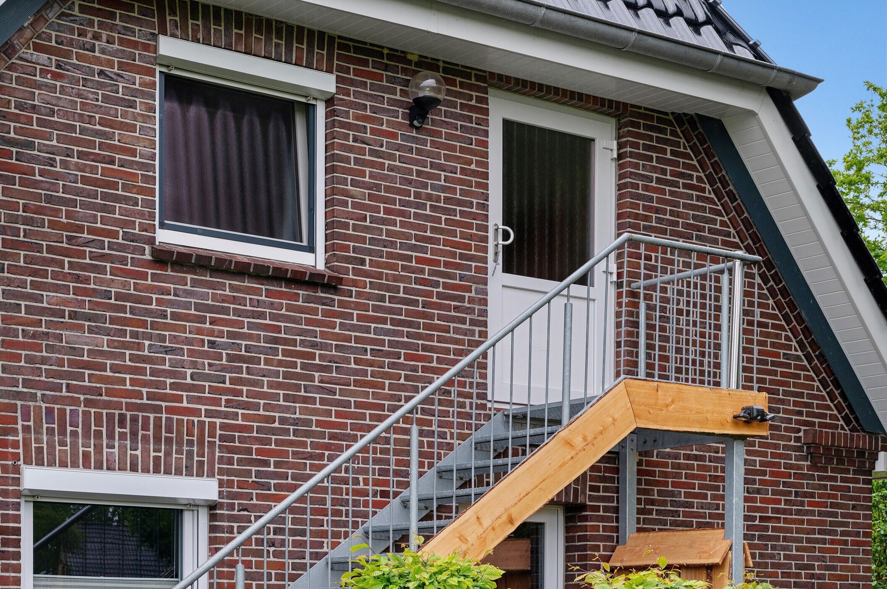 Un edificio de ladrillo con una escalera de madera, una ventana y una puerta.