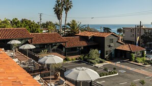 A hotel with a red-tiled roof, outdoor seating with umbrellas, and a view of the ocean. - Woods Cove Inn (Laguna Beach)