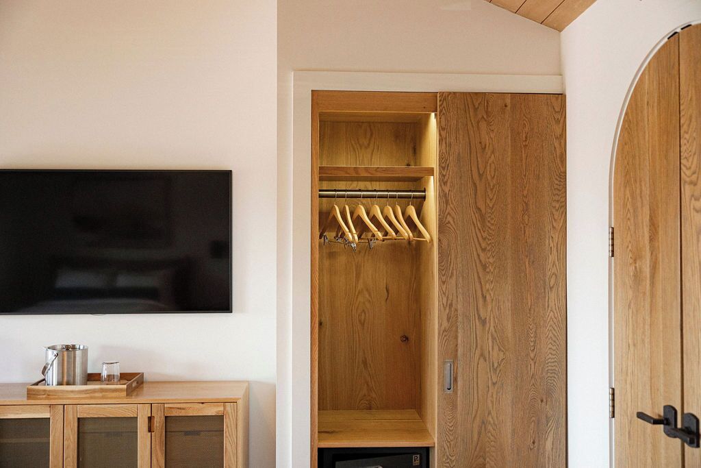 Un placard en bois avec une tringle pour suspendre les vêtements, un téléviseur à écran plat fixé au mur et un meuble en bois en dessous.