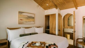 A bedroom with a large bed, a wooden ceiling, a painting, a wooden wardrobe, and a bathroom visible through an open door. - Woods Cove Inn (Laguna Beach)
