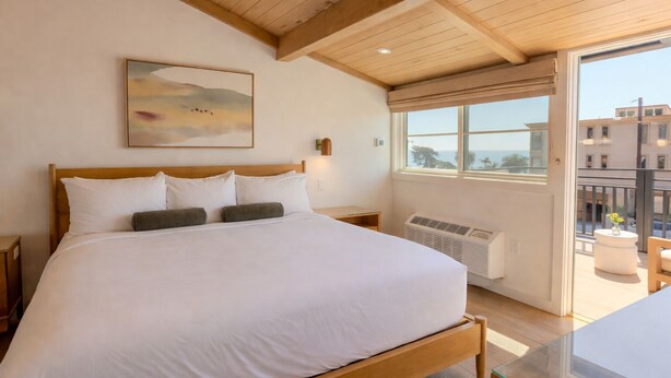 A bedroom with a wooden bed, a large window, and a view of the outside. - Woods Cove Inn (Laguna Beach)