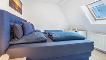 Een slaapkamer met een bed, kussens, een nachtkastje, een raam en een foto aan de muur.