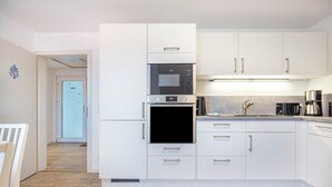 Una cocina moderna con armarios blancos, horno empotrado y cafetera.