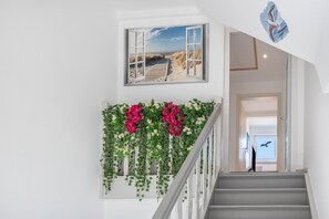 A staircase with a railing, a wall-mounted picture of a beach, and a wall-mounted bird decal.