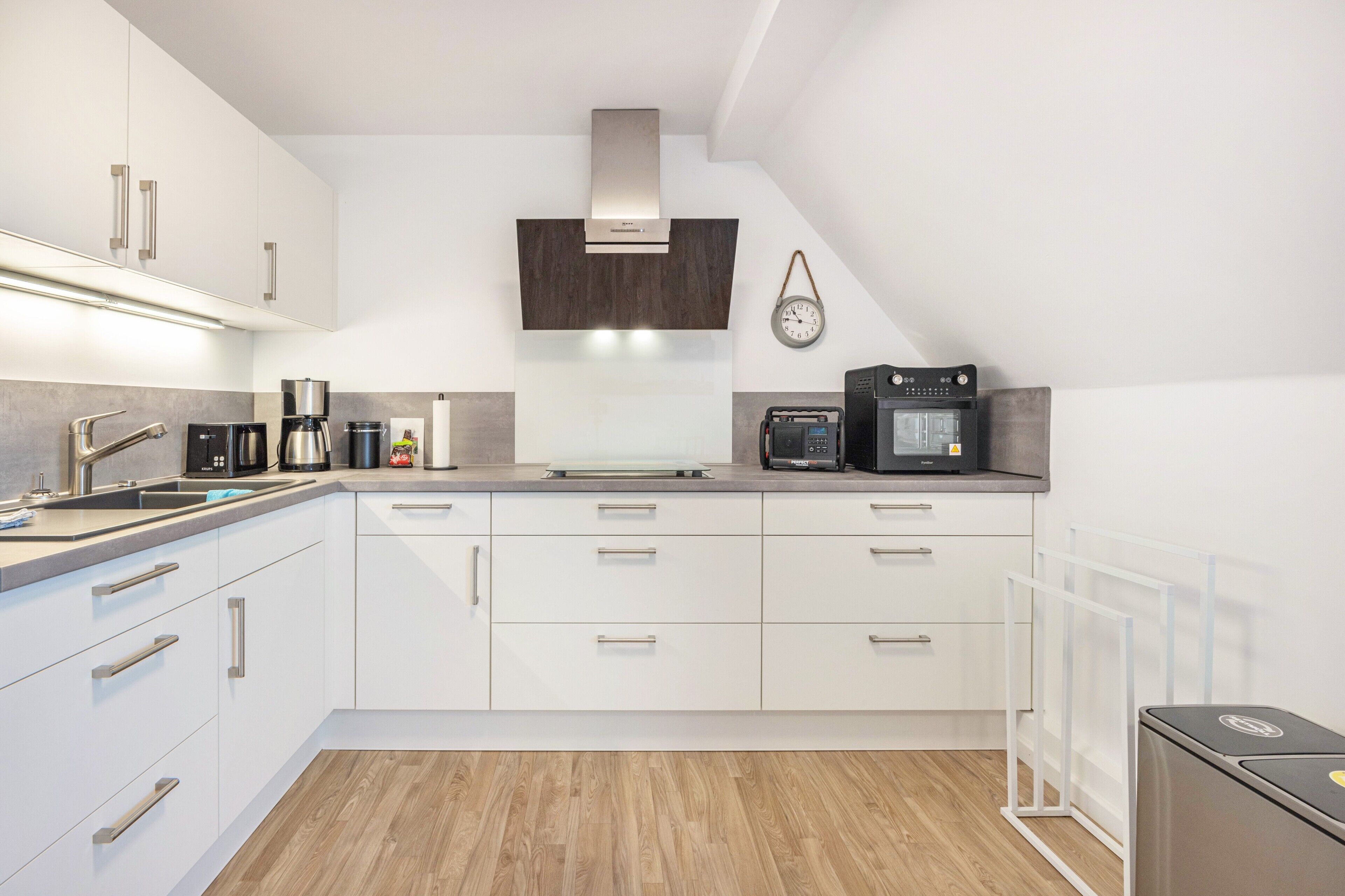 Una cocina moderna con gabinetes blancos, electrodomésticos de acero inoxidable y piso de madera.