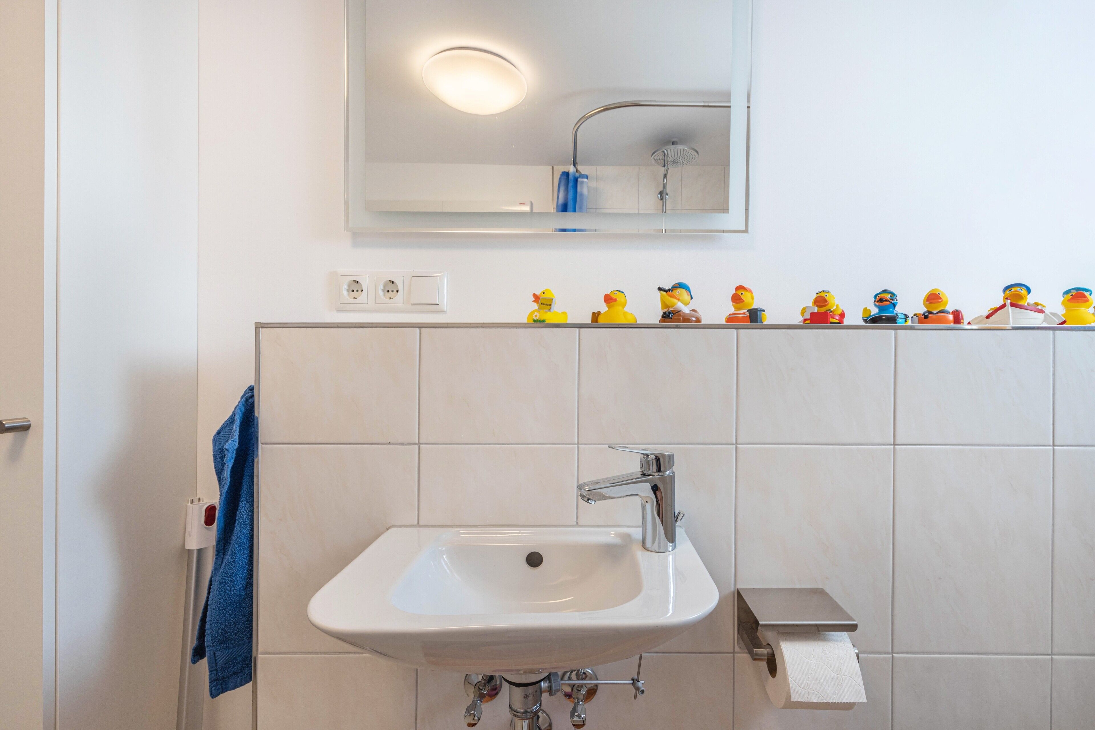 A bathroom with a white sink, a mirror, and a row of rubber duck toys on the wall.