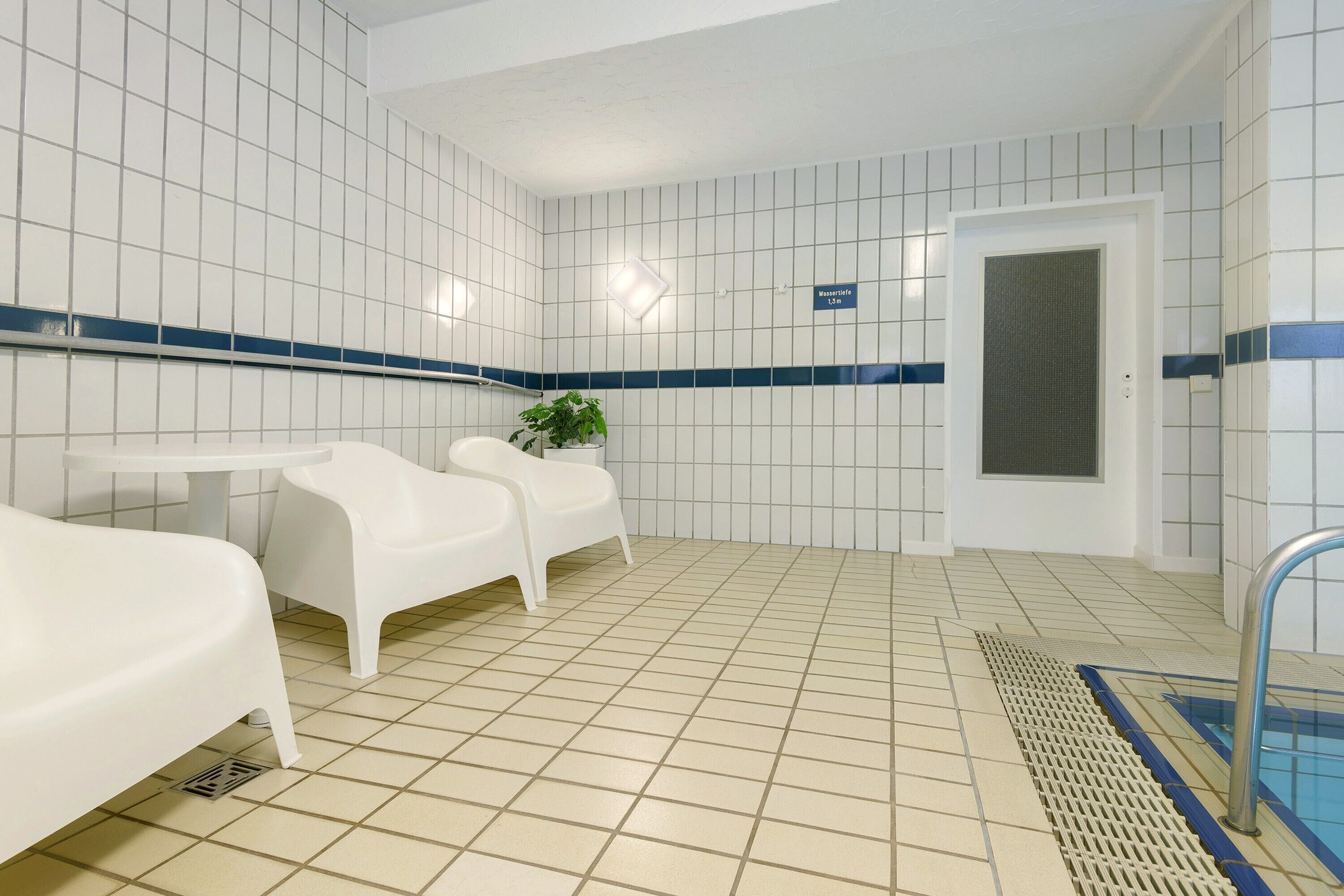 Une pièce propre, carrelée, avec une piscine, des chaises blanches et une petite table.