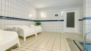 Une pièce propre, carrelée, avec une piscine, des chaises blanches et une petite table.