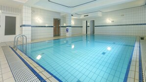 Una piscina interior amb parets de rajola, un fons de piscina blau i una barana.