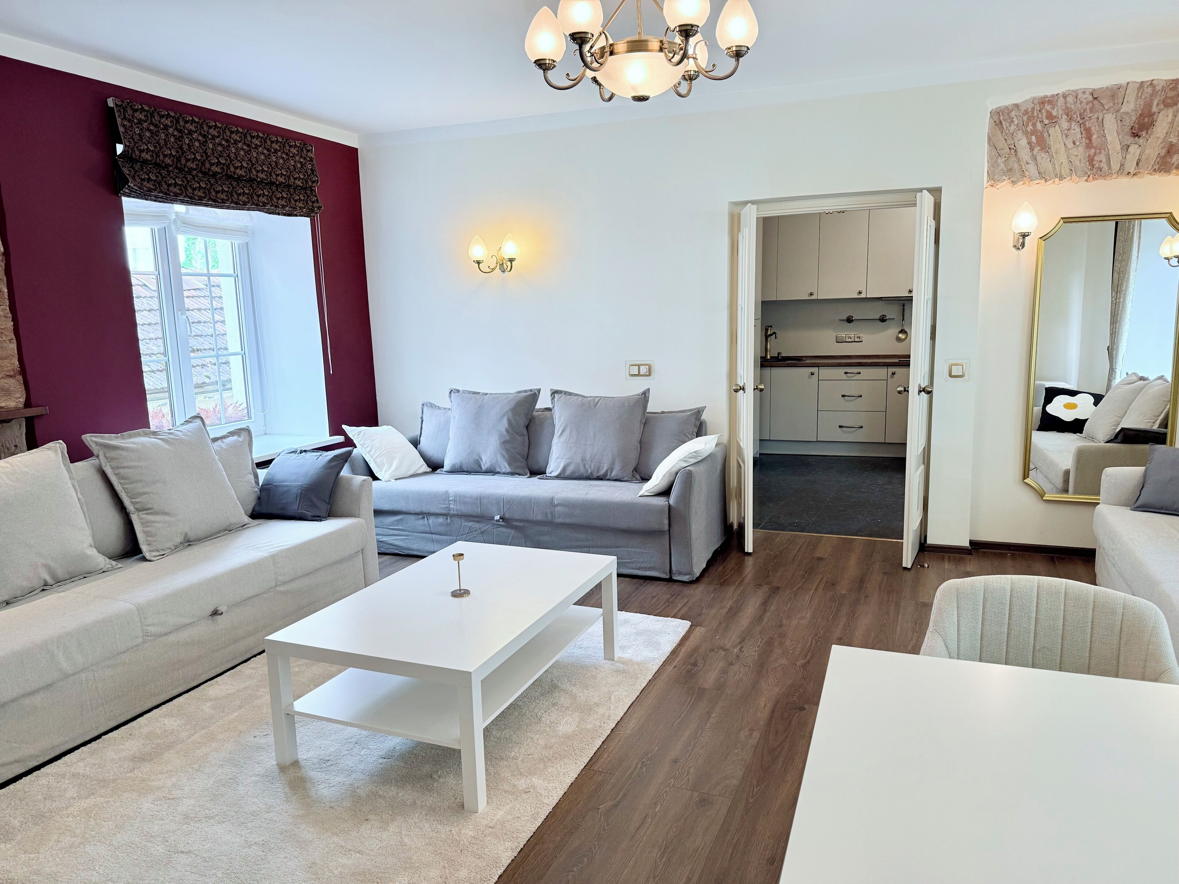 Un salon moderne avec un canapé gris, une table basse blanche et une cuisine visible à travers une porte ouverte.