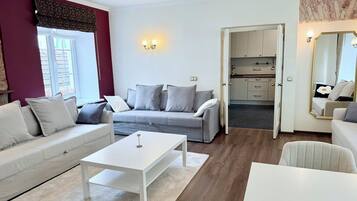 Un salon moderne avec un canapé gris, une table basse blanche et une cuisine visible à travers une porte ouverte.