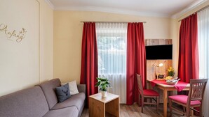 A living room with a sofa, a small wooden table, a TV, and a dining area with chairs. - Apartment 'Komfort  Römersberger - 1' with Wi-Fi (Vogtareuth)