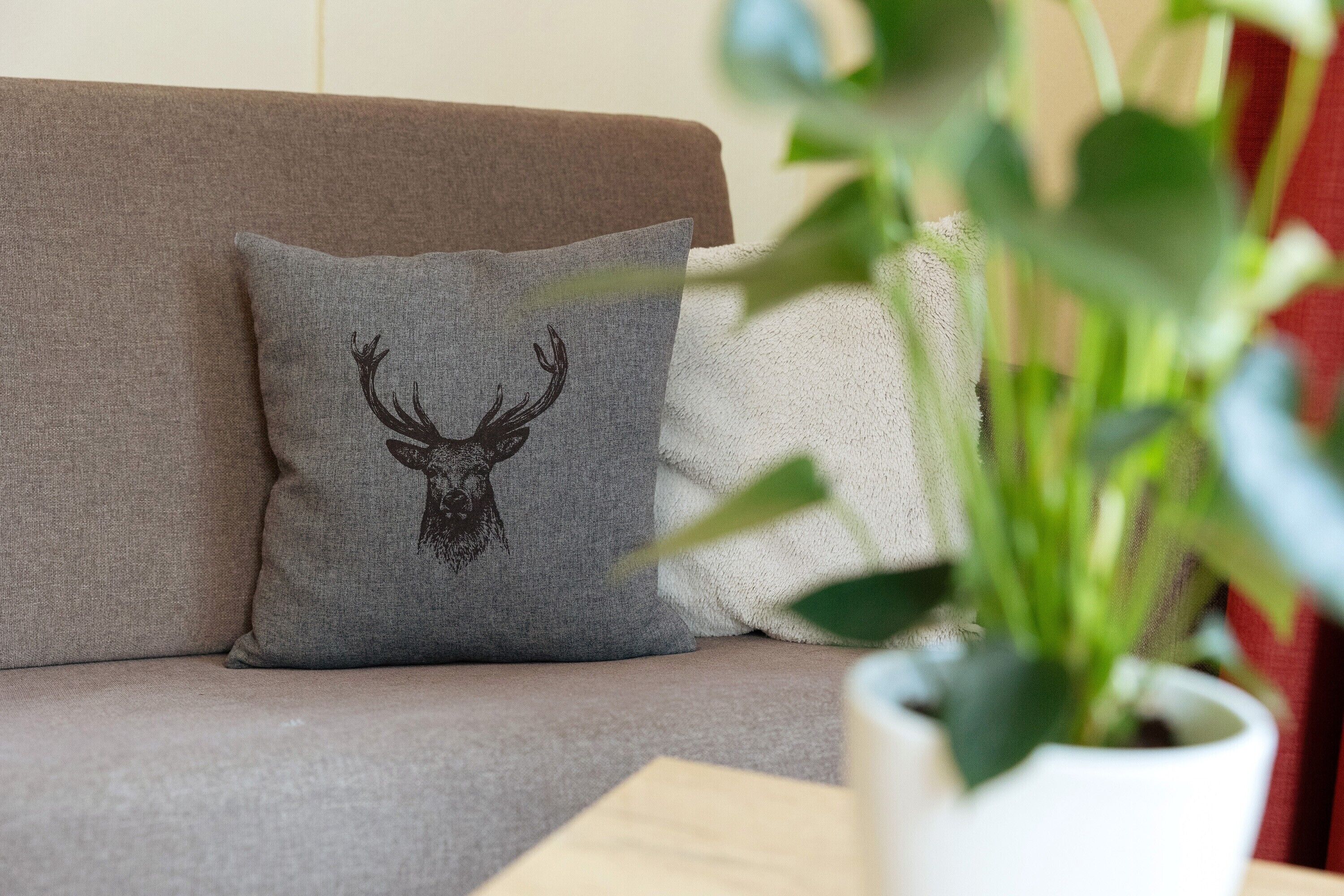 Un canapé avec un coussin orné de la silhouette d’un cerf, une plante en pot et un coussin blanc.