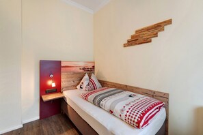 Ein Einzelbett mit Holz-Kopfteil, ein Nachttisch mit Lampe und ein an der Wand hängendes Kunstwerk.