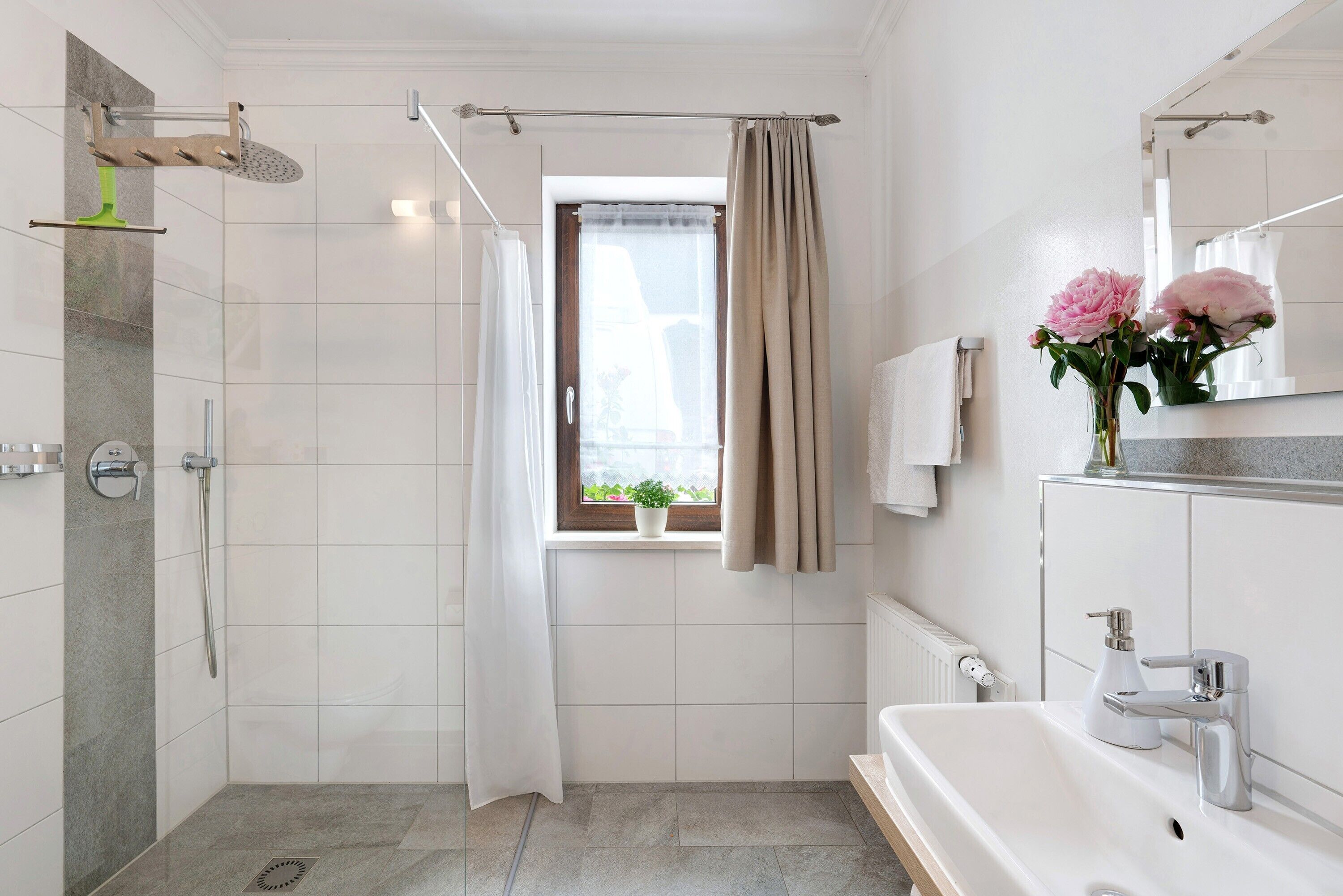 Un baño con ducha, lavabo, espejo y ventana con cortina.