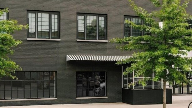 A modern building with a flat facade, multiple windows, and a small entrance area with a covered seating space. - The Industrialist Belvilla District 6 Formerly Sonder (Brooklyn)
